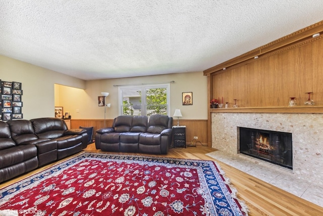 living room featuring a wainscoted wall, wood finished floors, wooden walls, a tile fireplace, and a textured ceiling