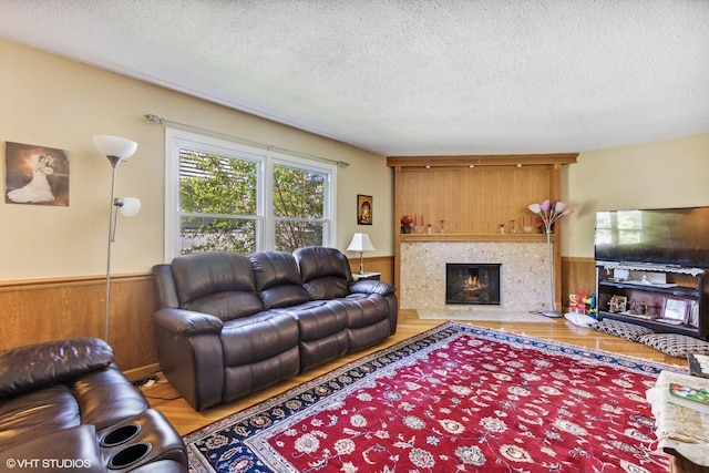 living room with wainscoting, a fireplace, wood finished floors, and a textured ceiling