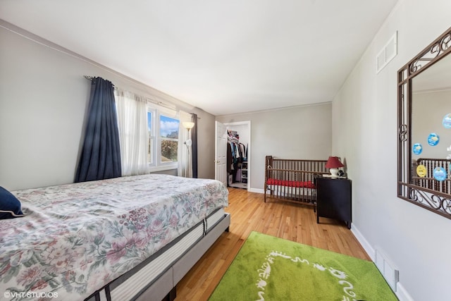 bedroom featuring light wood finished floors, a closet, a walk in closet, and baseboards