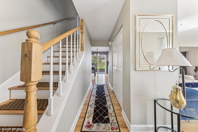 staircase featuring wood finished floors, baseboards, and a chandelier