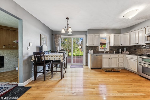 kitchen with stainless steel appliances, light wood finished floors, a chandelier, and backsplash