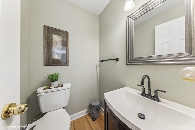 half bathroom with toilet, wood finished floors, vanity, and baseboards