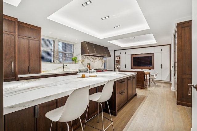 209 E Lake Shore Dr Unit 3W, Chicago, IL 60611 - kitchen featuring a raised ceiling, wall chimney range hood, a sink, a breakfast bar, and light stone countertops