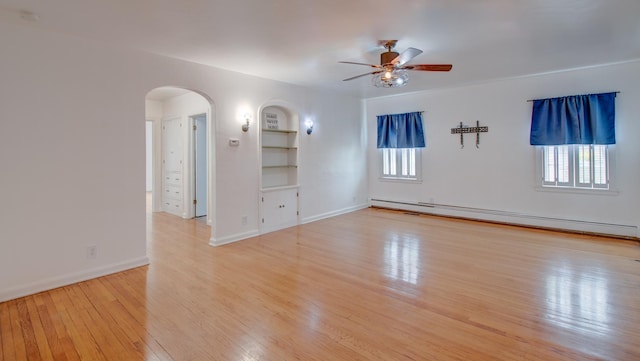 110 N Newton St, Goodland, IN 47948 - empty room featuring a baseboard heating unit, arched walkways, ceiling fan, light wood-style floors, and built in shelves