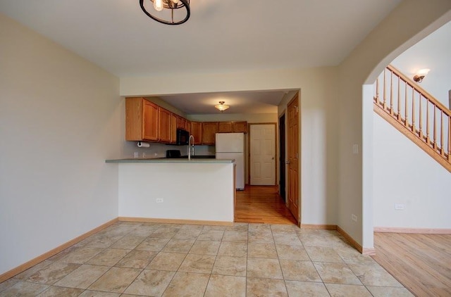1716 Waters Edge Dr Unit 1716, Minooka, IL 60447 - kitchen with freestanding refrigerator, arched walkways, a peninsula, baseboards, and brown cabinetry