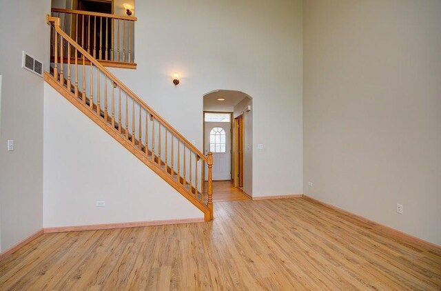 1716 Waters Edge Dr Unit 1716, Minooka, IL 60447 - unfurnished living room featuring arched walkways, wood finished floors, a towering ceiling, stairs, and baseboards