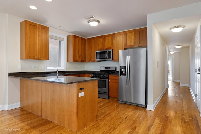 25 E 26th St Unit 4, Chicago, IL 60616 - kitchen with appliances with stainless steel finishes, a peninsula, light wood-style flooring, dark stone countertops, and brown cabinetry