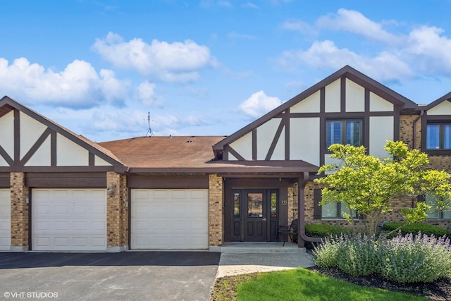 tudor-style house featuring stucco siding, asphalt driveway, a garage, and roof with shingles