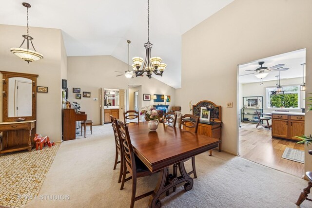 dining area featuring a ceiling fan, a chandelier, light colored carpet, and high vaulted ceiling