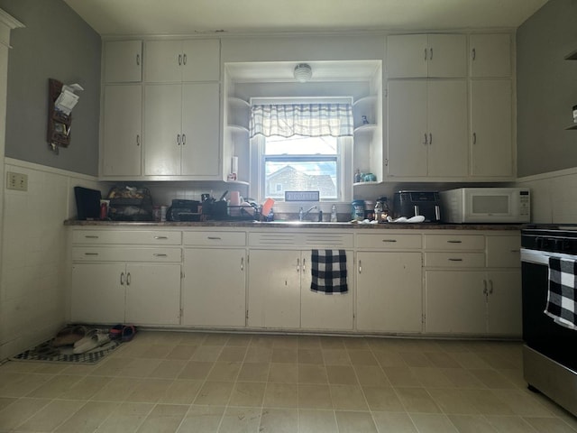 1309 S Main St, Bloomington, IL 61701 - kitchen with open shelves, white microwave, stainless steel gas range oven, white cabinets, and a wainscoted wall