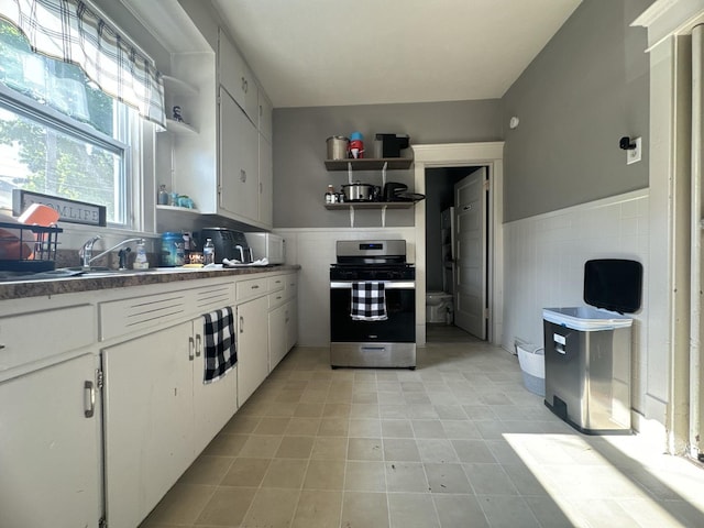 1309 S Main St, Bloomington, IL 61701 - kitchen with open shelves, stainless steel range with gas stovetop, tile walls, a wainscoted wall, and white cabinets