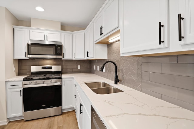 2034 W 75th Pl Unit 32, Merrillville, IN 46410 - kitchen featuring appliances with stainless steel finishes, a sink, white cabinetry, light wood-type flooring, and backsplash