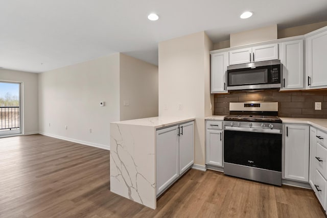 2034 W 75th Pl Unit 32, Merrillville, IN 46410 - kitchen featuring stainless steel appliances, a peninsula, wood finished floors, decorative backsplash, and recessed lighting