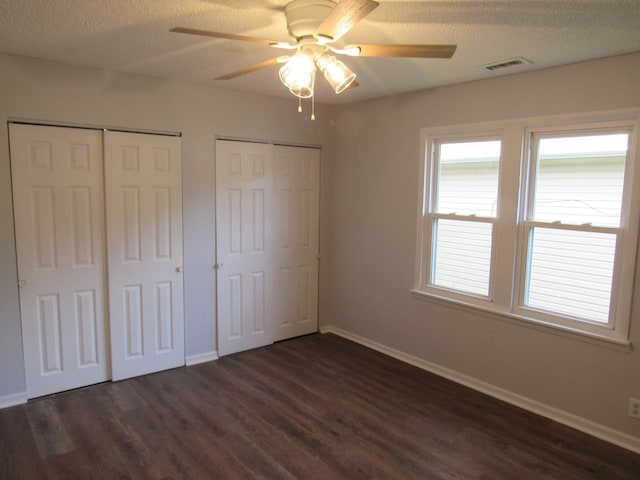 1503 Cherokee Dr, Round Lake Beach, IL 60073 - unfurnished bedroom featuring multiple closets, dark wood-type flooring, baseboards, a textured ceiling, and a ceiling fan