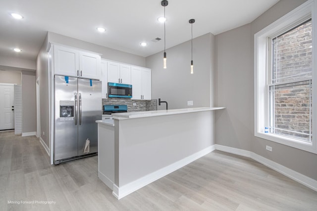 3926 W Arthington St, Chicago, IL 60624 - kitchen featuring appliances with stainless steel finishes, light wood-type flooring, white cabinetry, a peninsula, and decorative light fixtures