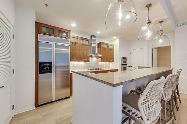 500 W Superior St Unit 612, Chicago, IL 60654 - kitchen with stainless steel appliances, wall chimney exhaust hood, brown cabinetry, light wood-style floors, and decorative backsplash