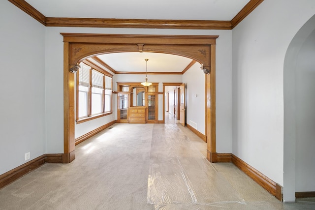 hallway featuring arched walkways, crown molding, baseboards, and carpet floors
