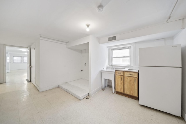 kitchen featuring freestanding refrigerator, brown cabinets, light countertops, and light floors