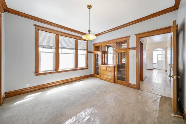 unfurnished dining area with carpet floors, arched walkways, crown molding, and baseboards