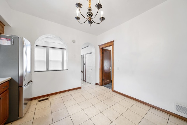 unfurnished dining area with a chandelier, arched walkways, baseboards, and light tile patterned floors