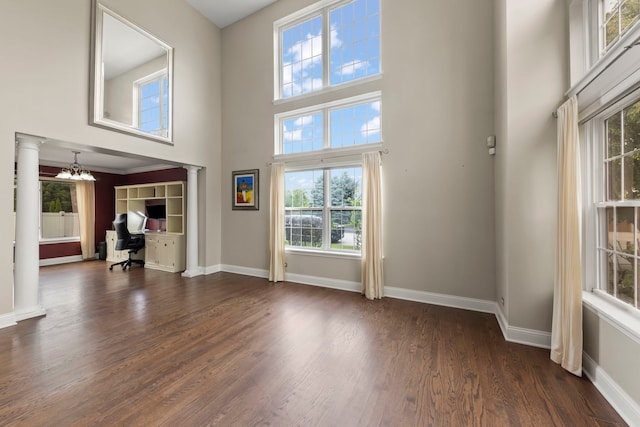 1462 Haversham Dr, Aurora, IL 60502 - unfurnished living room featuring ornate columns, a towering ceiling, a desk, dark wood-type flooring, and baseboards