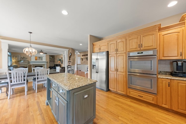 10423 Capistrano Ln, Orland Park, IL 60467 - kitchen with stainless steel appliances, a center island, light stone counters, light wood-type flooring, and wainscoting