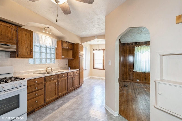 10624 S Ave H Rd, Chicago, IL 60617 - kitchen featuring white range with gas cooktop, under cabinet range hood, brown cabinets, a sink, and a textured ceiling