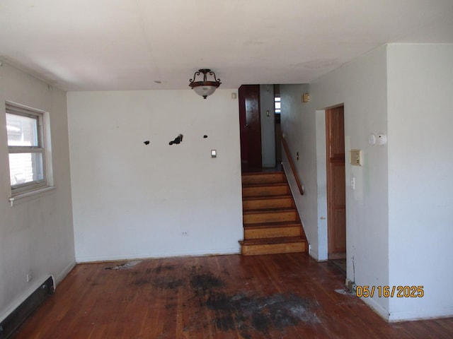 unfurnished room featuring wood finished floors, stairway, baseboards, and a baseboard radiator