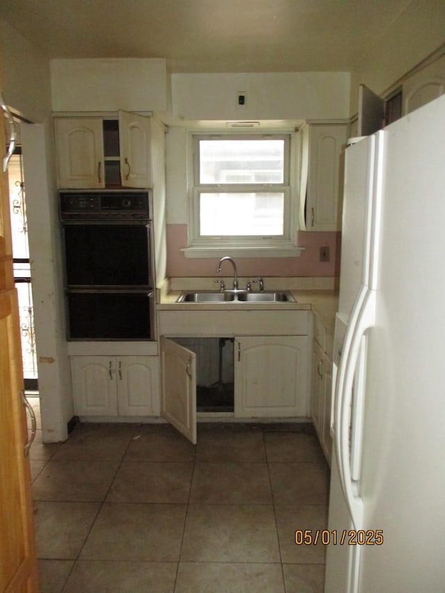 kitchen featuring freestanding refrigerator, light countertops, light tile patterned floors, a sink, and white cabinets