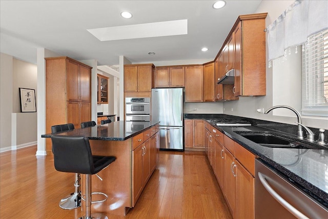 13093 Timber Ct Unit 61, Palos Heights, IL 60463 - kitchen featuring appliances with stainless steel finishes, a skylight, a breakfast bar area, under cabinet range hood, and light wood-style floors