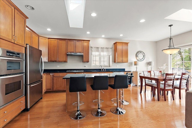 13093 Timber Ct Unit 61, Palos Heights, IL 60463 - kitchen with appliances with stainless steel finishes, brown cabinetry, a kitchen breakfast bar, light wood finished floors, and a center island