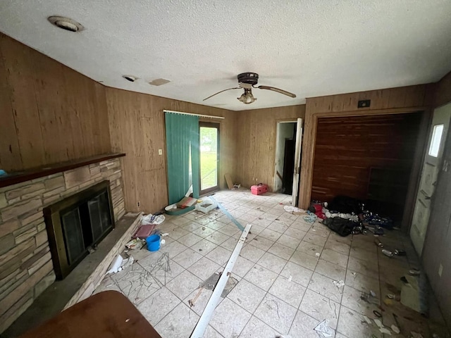 103 W 2nd St, Broadlands, IL 61816 - unfurnished living room with a stone fireplace, a textured ceiling, wooden walls, and a ceiling fan