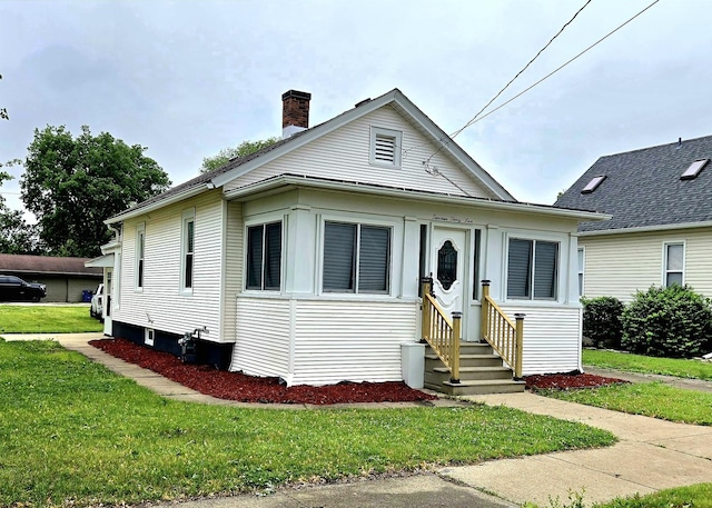 view of front facade with entry steps, a front lawn, and a chimney
