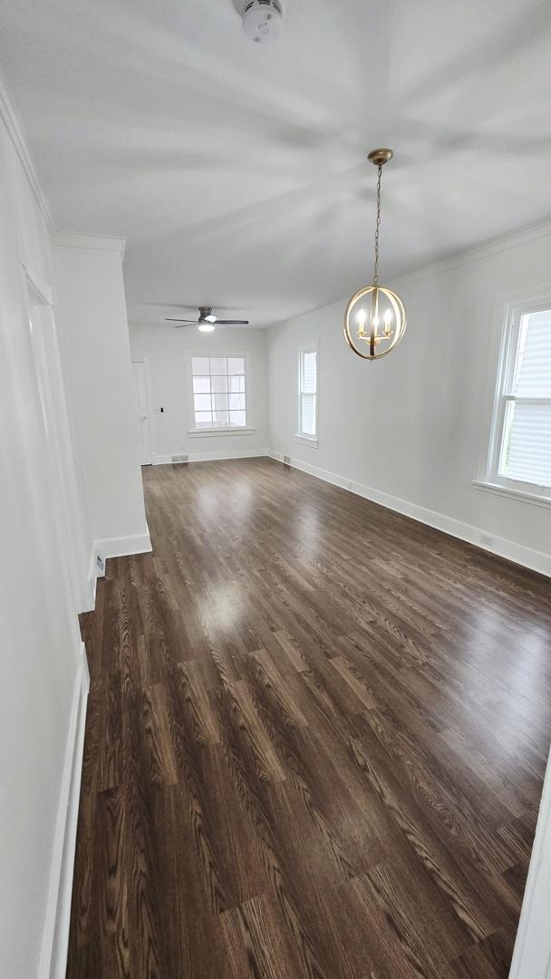 empty room featuring dark wood-style floors, baseboards, a chandelier, crown molding, and ceiling fan
