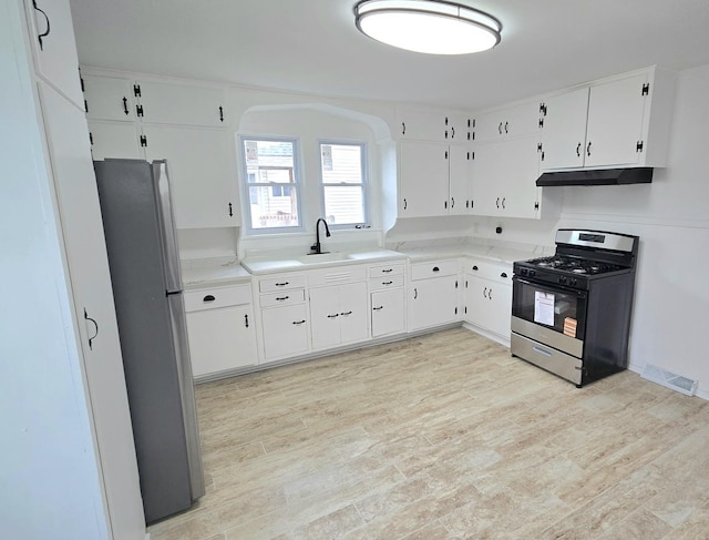 kitchen featuring gas stove, under cabinet range hood, freestanding refrigerator, light wood-style flooring, and a sink
