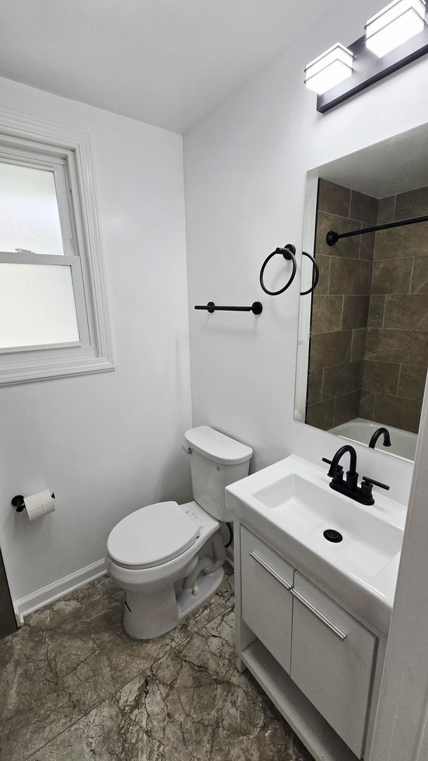 full bath featuring vanity, toilet, tiled shower, and baseboards