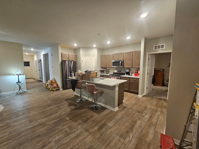 6321 Aspen Ln, Wonder Lake, IL 60097 - kitchen featuring stainless steel appliances, dark wood-style flooring, a center island with sink, a breakfast bar area, and light countertops