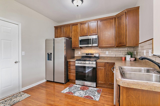 101 E Robinson Ave, Cortland, IL 60112 - kitchen featuring stainless steel appliances, a sink, brown cabinetry, backsplash, and light wood-type flooring