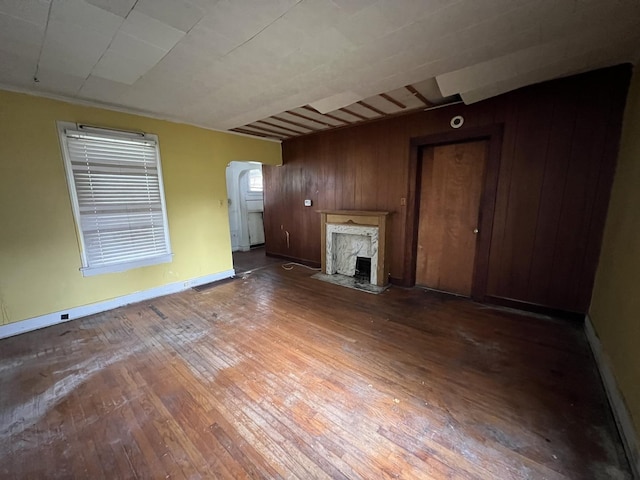 unfurnished living room featuring arched walkways, hardwood / wood-style flooring, a high end fireplace, wooden walls, and baseboards