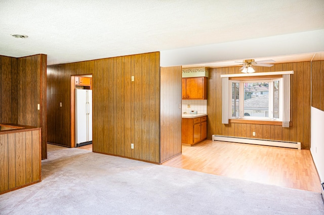 207 Muehl Dr, Lockport, IL 60441 - unfurnished living room with a baseboard radiator, light carpet, wooden walls, ceiling fan, and light wood-style flooring
