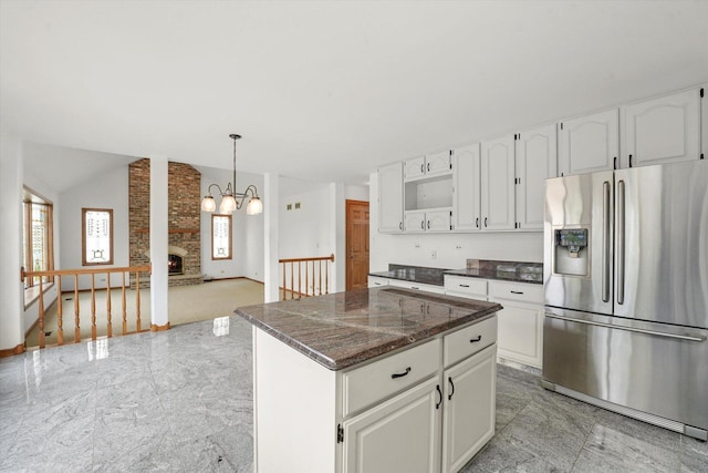 kitchen with stainless steel fridge, light marble finish floors, white cabinets, a fireplace, and lofted ceiling