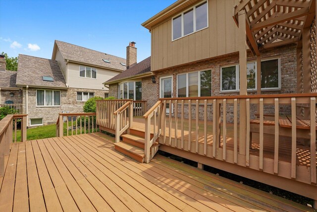 rear view of house featuring brick siding, a wooden deck, a yard, and a chimney