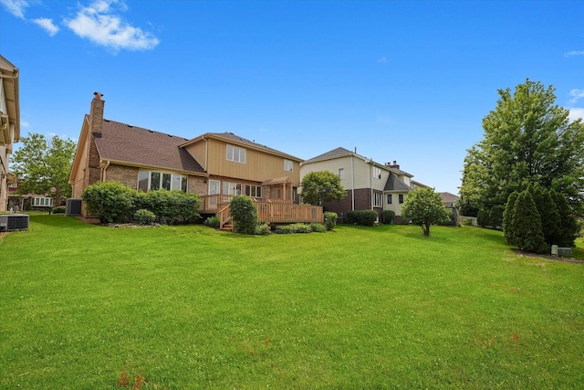 rear view of property featuring a chimney, a lawn, a deck, and brick siding