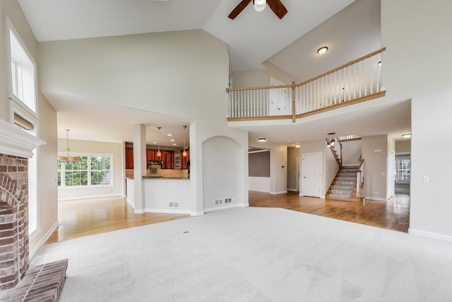 12354 S Blue Water Pkwy, Plainfield, IL 60585 - unfurnished living room with carpet flooring, stairs, a brick fireplace, a ceiling fan, and high vaulted ceiling