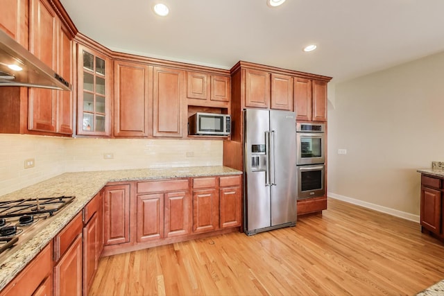 12354 S Blue Water Pkwy, Plainfield, IL 60585 - kitchen featuring stainless steel appliances, wall chimney exhaust hood, light wood finished floors, tasteful backsplash, and glass insert cabinets