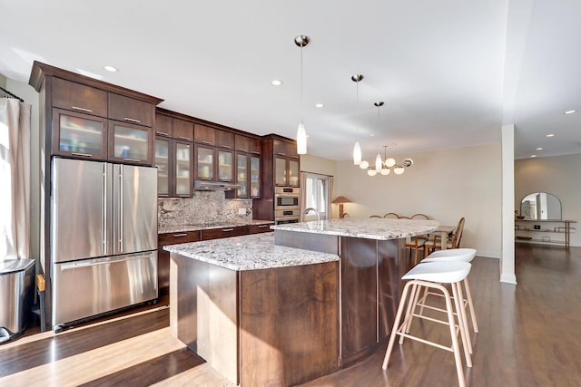 5843 N Oconto Ave, Chicago, IL 60631 - kitchen featuring appliances with stainless steel finishes, dark brown cabinets, an island with sink, dark wood-style flooring, and under cabinet range hood