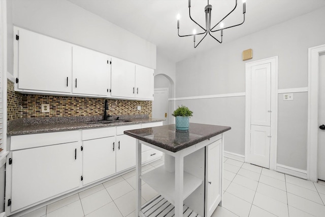 5331 W Schubert Ave, Chicago, IL 60639 - kitchen featuring decorative backsplash, light tile patterned floors, white cabinets, arched walkways, and a chandelier