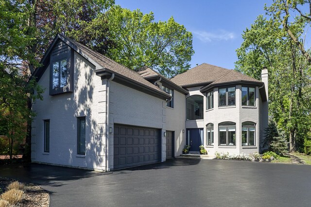 244 Kenmore Ave, Deerfield, IL 60015 - french country style house with asphalt driveway, brick siding, a chimney, a shingled roof, and an attached garage
