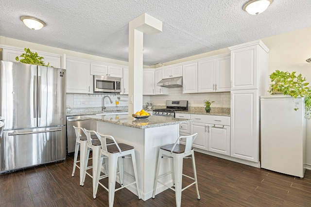 2211 S Highland Ave Unit 1B, Lombard, IL 60148 - kitchen featuring stainless steel appliances, under cabinet range hood, a sink, a kitchen bar, and dark wood-style floors