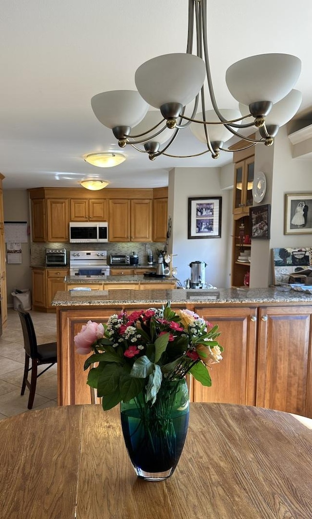 7033 N Kedzie Ave Unit 301, Chicago, IL 60645 - kitchen featuring stainless steel range with electric stovetop, white microwave, brown cabinets, backsplash, and a chandelier